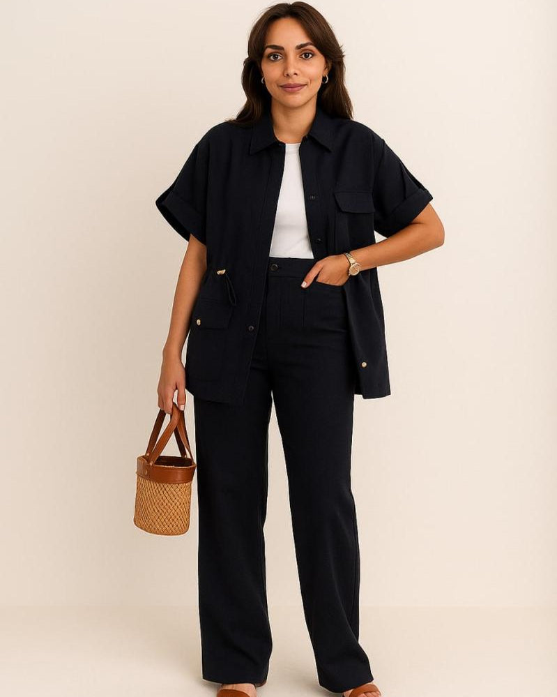 Woman wearing a black outfit with a white top, holding a woven bag against a beige background