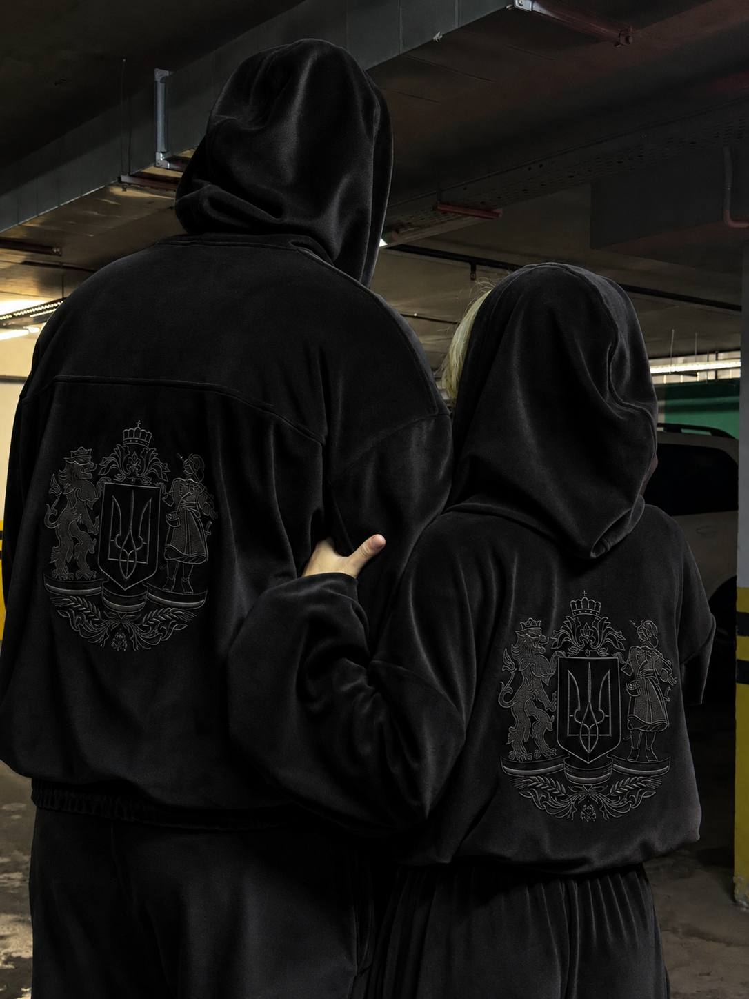 Man wearing black velour tracksuit with embroidered Ukrainian coat of arms on the back