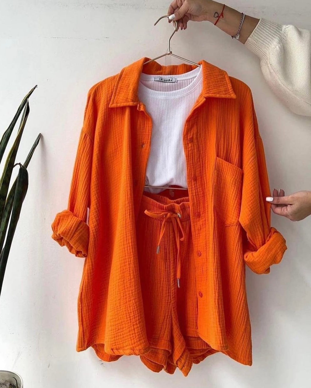 Orange shirt and shorts set on a hanger against a white background