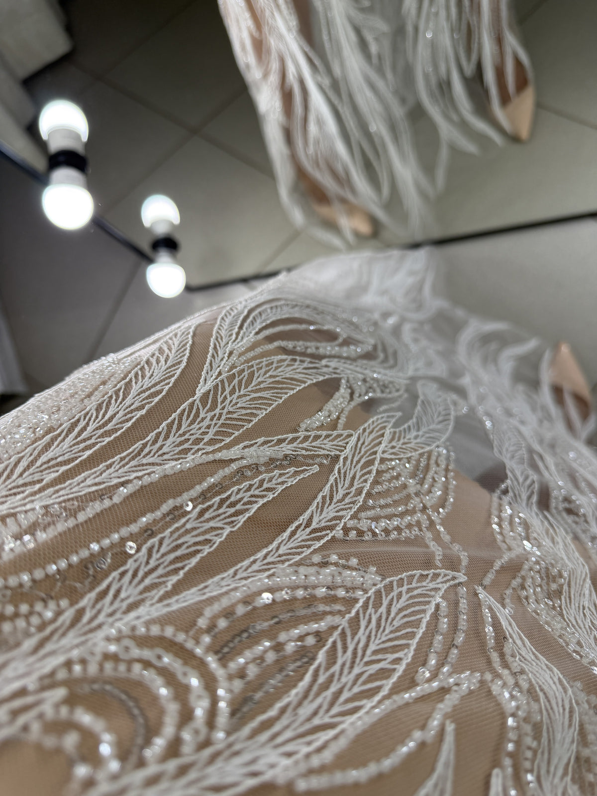Macro detail of white guipure embroidery with beads and sequins on beige crepe base