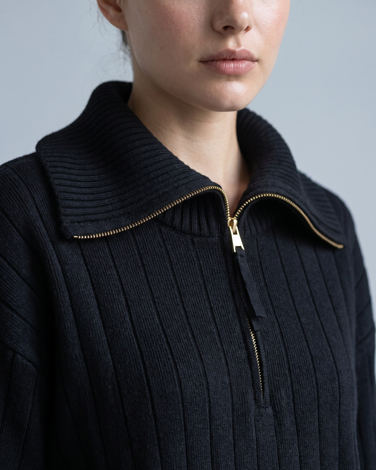 Nahaufnahme des goldenen Halbreißverschluss-Zippers am Kragen eines schwarzen Sweatshirts aus Rippstrick
