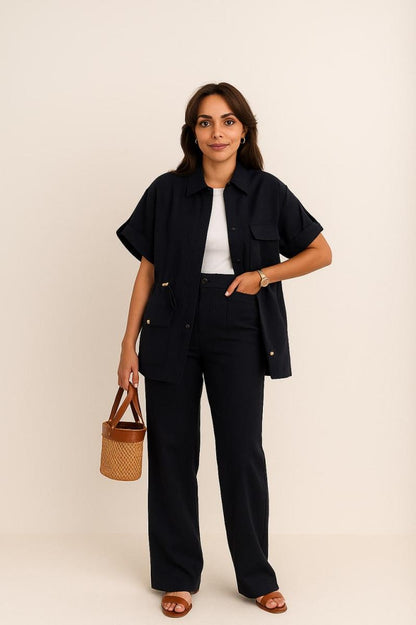 Woman wearing a black outfit with a white top, holding a woven bag against a beige background