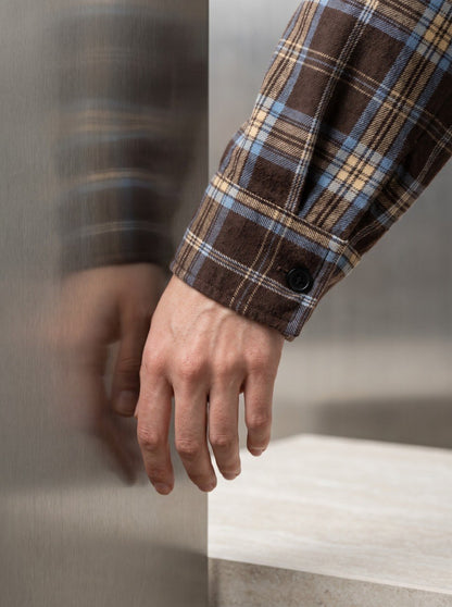 Close-up of a brown plaid flannel shirt's cuff with button detail on the sleeve
