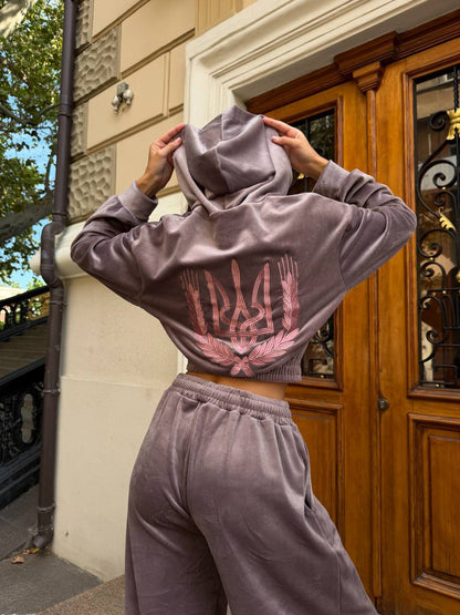 Close-up of the embroidered trident and wheat wreath design on a mauve velour tracksuit hoodie