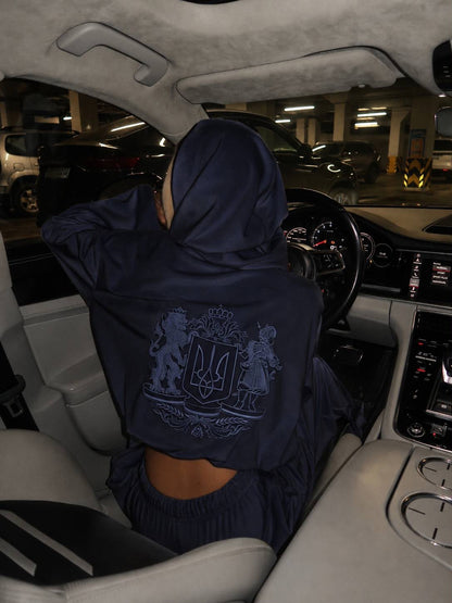 Woman wearing dark blue velour hoodie with Ukrainian coat of arms embroidery, hood up, back view in car