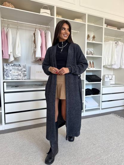 Charcoal gray ribbed knit long cardigan with self-tie belt, worn open over a black top and skirt, front view