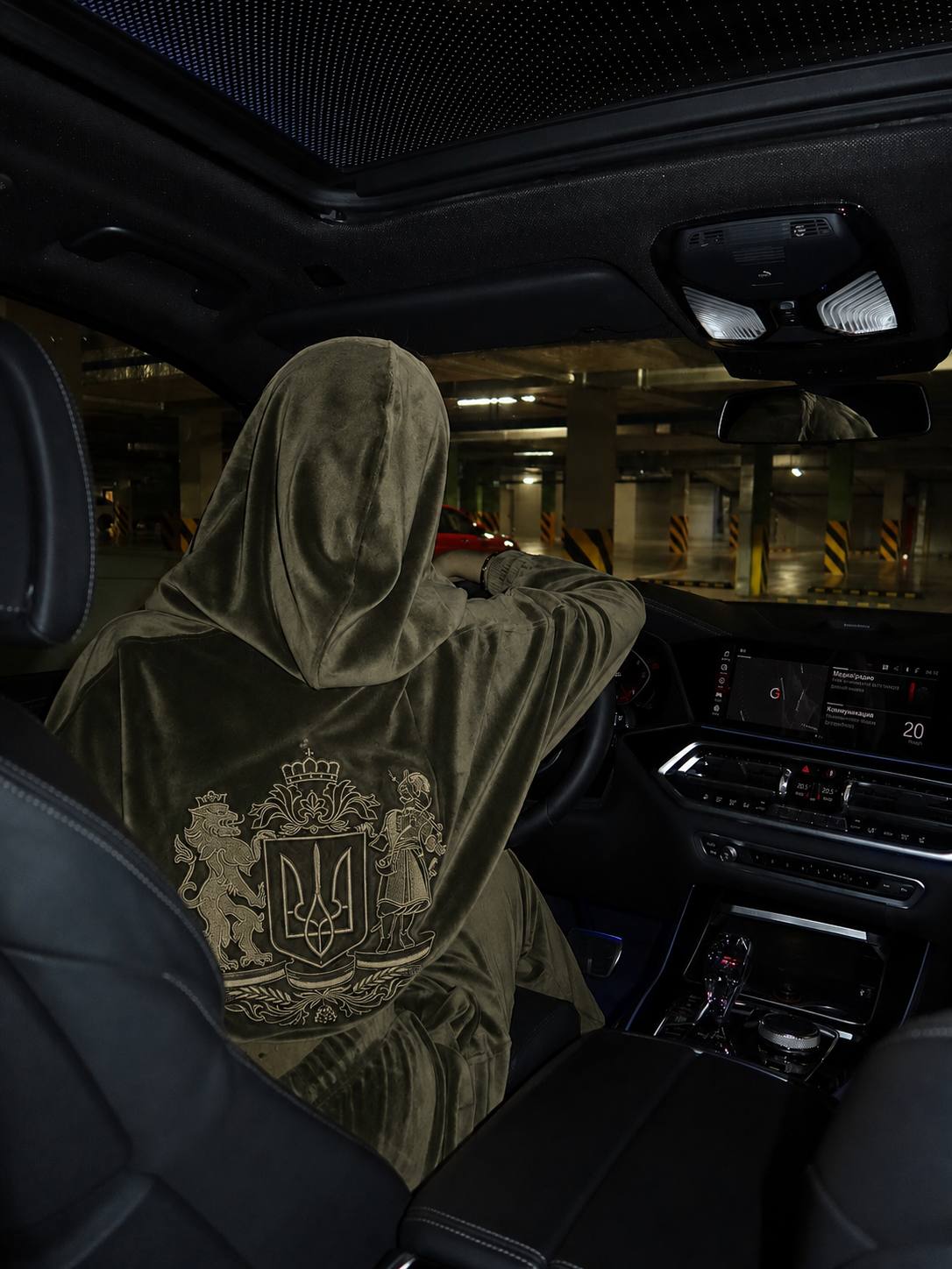 Side-back view of khaki velour hooded tracksuit with embroidered Ukrainian coat of arms, woman driving car