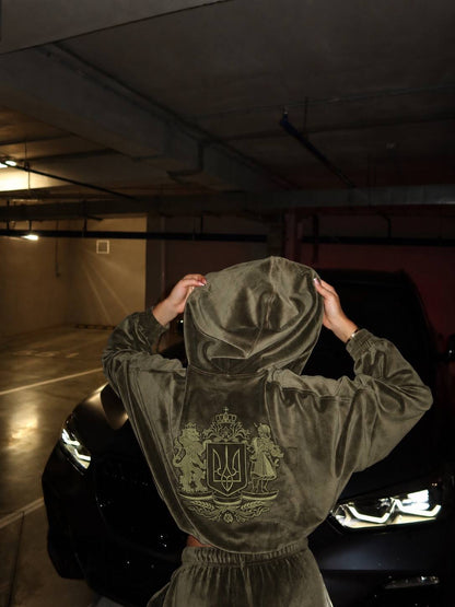 Woman adjusting hood of khaki velour tracksuit with Ukrainian coat of arms embroidery, back view in parking garage