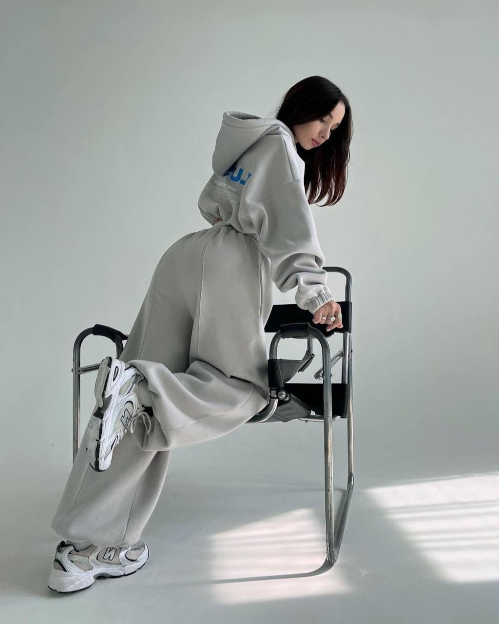 Gray hooded tracksuit and wide-leg trousers worn with chunky sneakers - side view on a chair