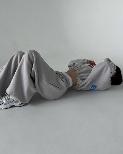 Gray oversized tracksuit - lying view showing the wide-leg trousers with side pockets and elastic cuffs