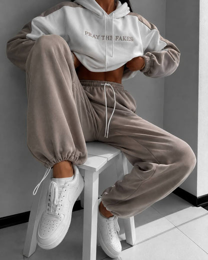 Milk-white hoodie with beige sleeves and beige joggers - seated on a white stool