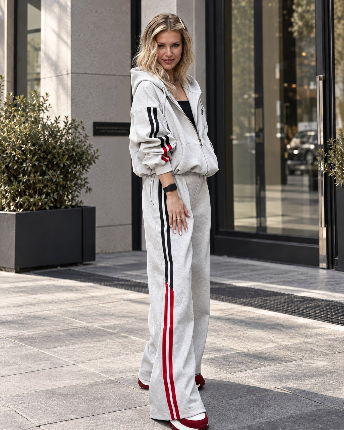 Light gray women's tracksuit - zip hoodie worn open over a black top and wide-leg trousers, three-quarter view
