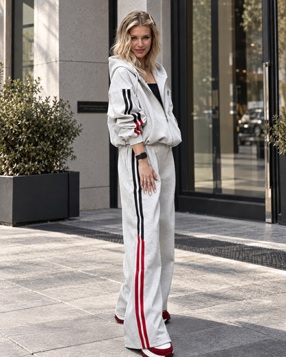 Light gray women's tracksuit - zip hoodie worn open over a black top and wide-leg trousers, three-quarter view