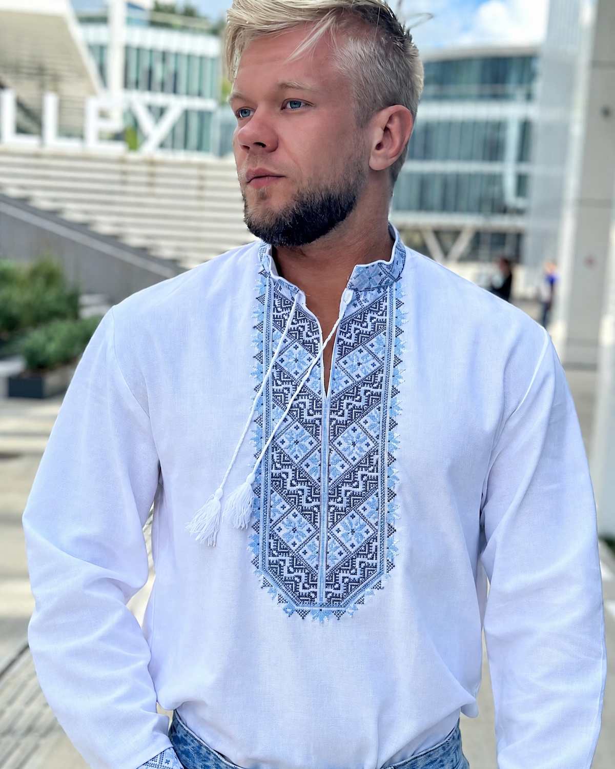Men's white cotton vyshyvanka with blue geometric embroidery, front view on a city street