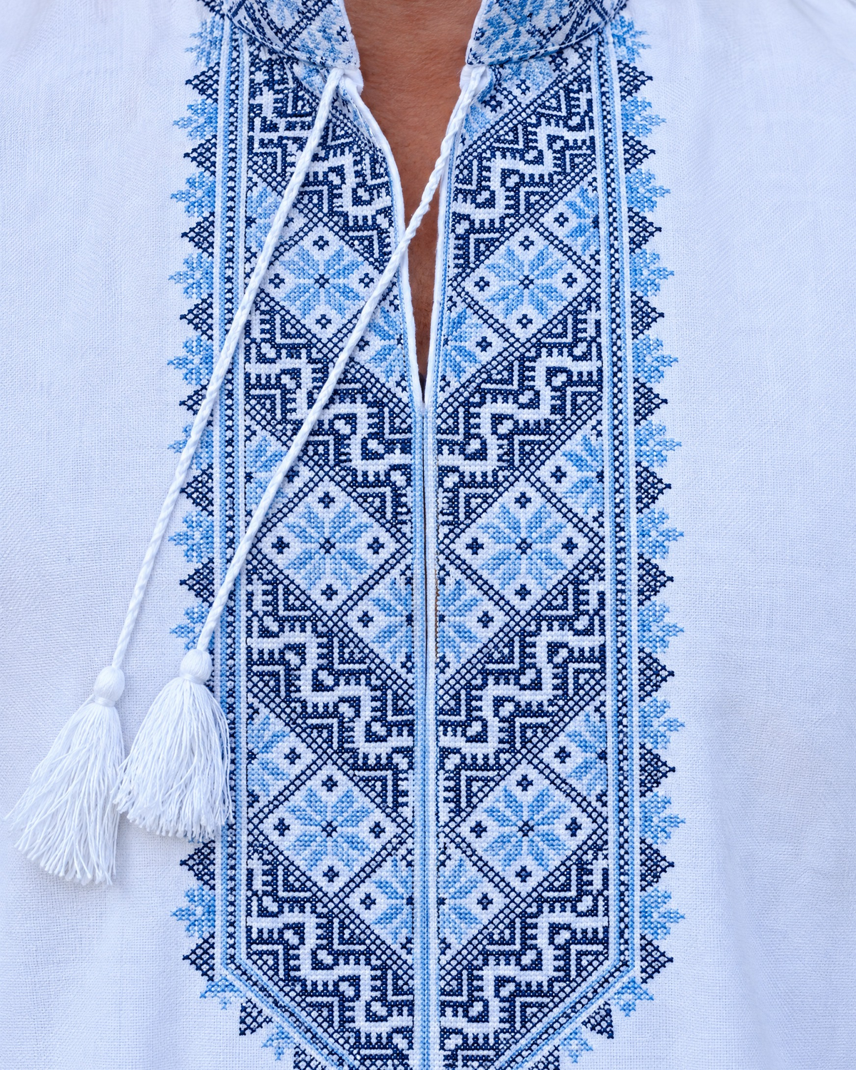 Close-up of blue and navy geometric embroidery on the collar and front panel of a men's white vyshyvanka with tassel ties