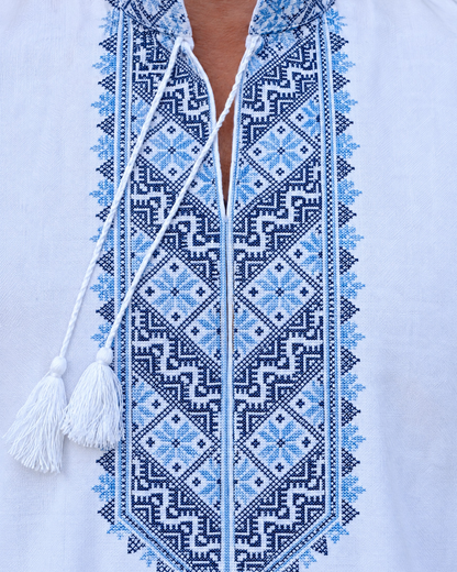 Close-up of blue and navy geometric embroidery on the collar and front panel of a men's white vyshyvanka with tassel ties