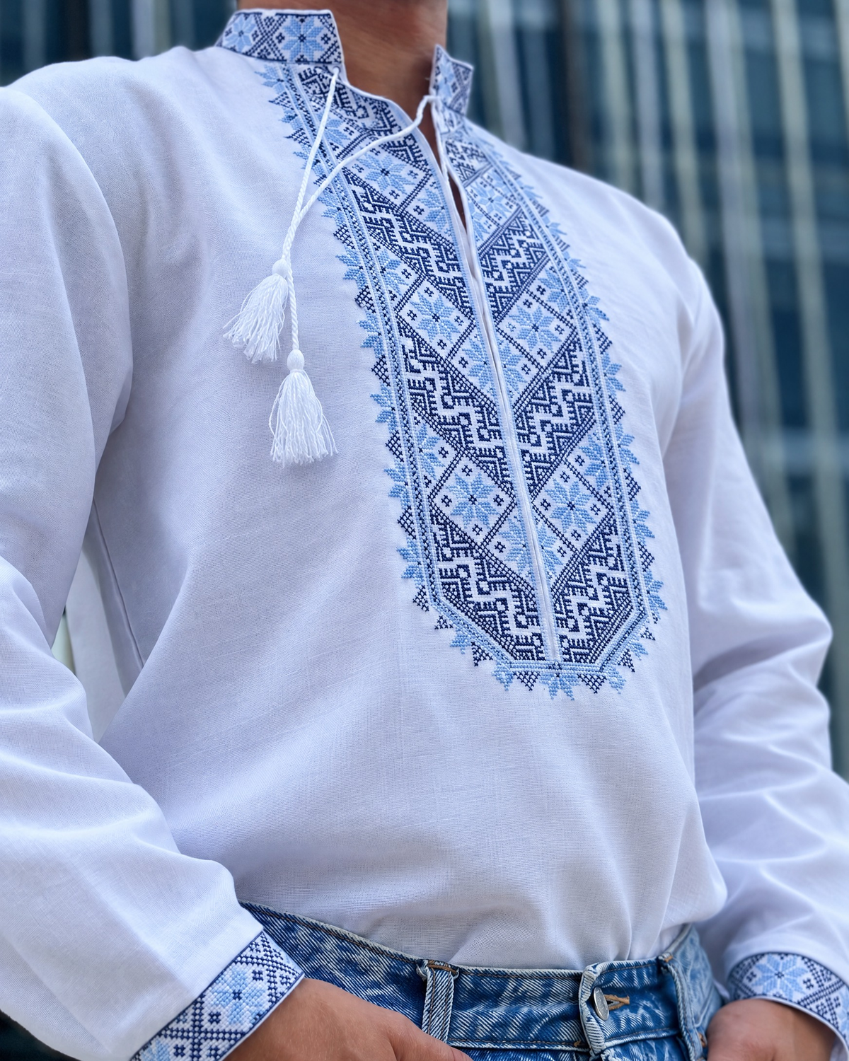 Men's long-sleeve vyshyvanka with blue embroidered front panel, stand collar and white tassel ties, three-quarter view