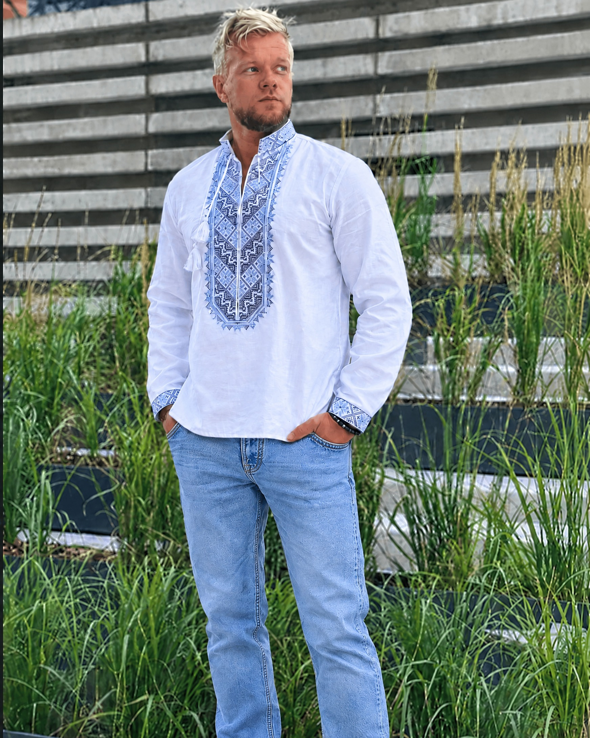 Man in a white long-sleeve vyshyvanka with blue embroidery and light blue jeans, full-length view