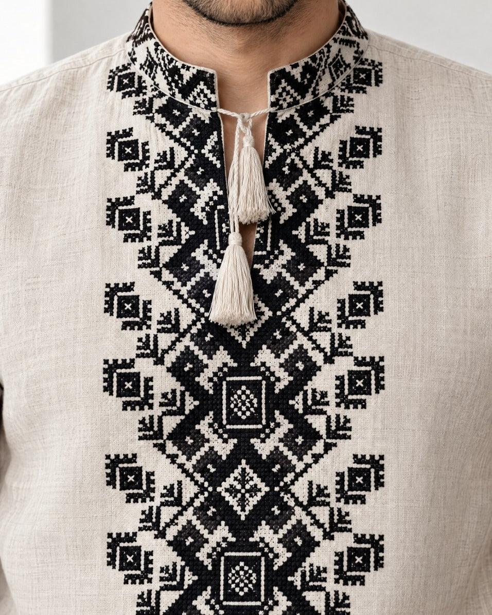 Close-up of black cross-stitch embroidery on the collar and chest of a men's linen vyshyvanka with tassel ties