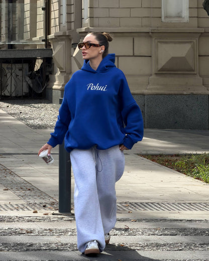 Blue oversized hoodie with white embroidery worn with light grey wide-leg trousers - full-length street look with a coffee cup