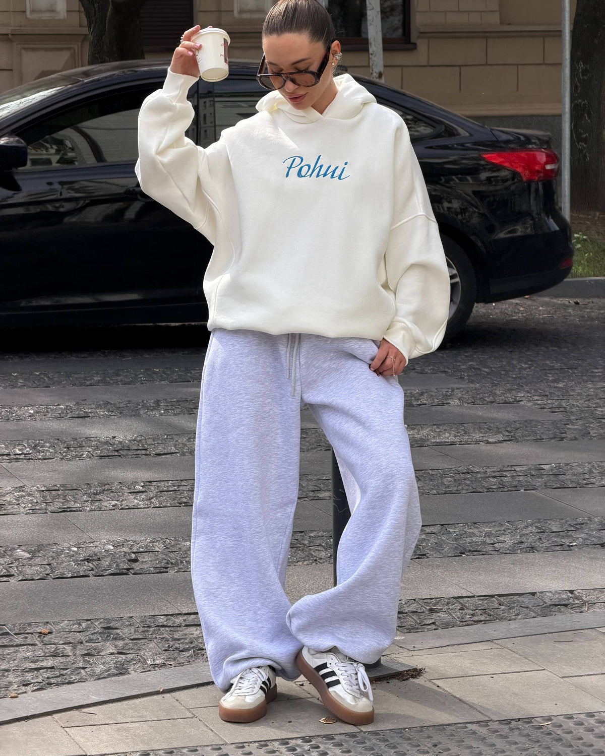 Milk-white oversized hoodie with blue embroidery worn with light grey trousers and sneakers - full-length street look