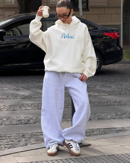 Milk-white oversized hoodie with blue embroidery worn with light grey trousers and sneakers - full-length street look