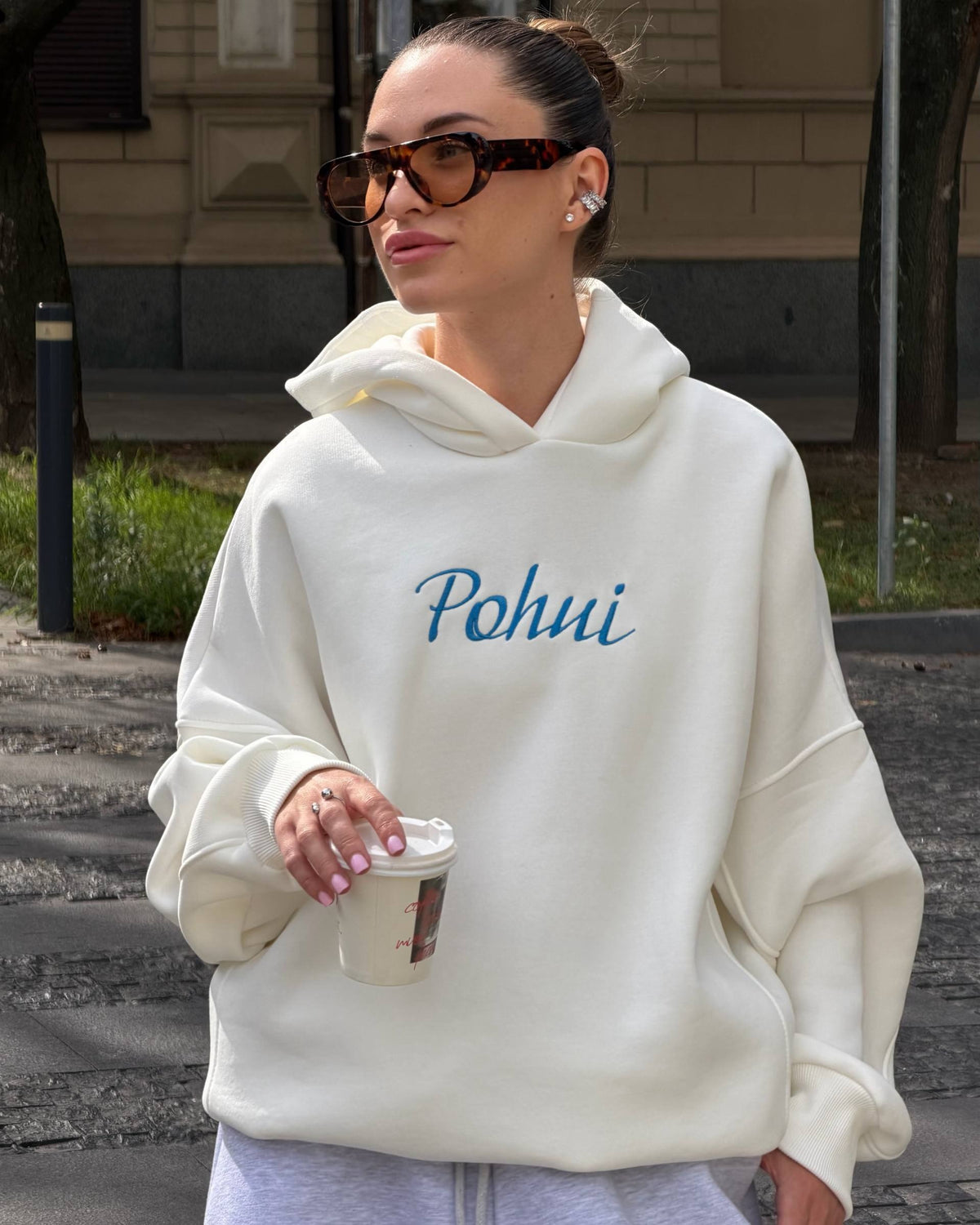 Milk-white fleece-lined hoodie with blue embroidery on the chest - portrait with sunglasses and a coffee cup