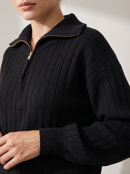 Close-up of black ribbed knit sweatshirt funnel collar with gold half-zip